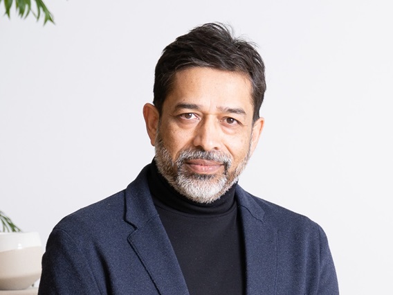Professional headshot of Asheesh Saksena wearing a black turtleneck shirt underneath a navy-blue sport coat.